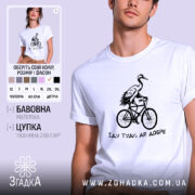 Футболка їду туди де добре, біла футболка на чоловікові, з принтом чорного кольору, на якому зображена лелека на велосипеді, фон світло-фіолетовий, деталі принта чіткі та контрастні.