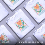 Футболка єдність і сила, біла футболка на моделі, з принтом квітів і написом 'COMMUNITY IS RESISTANCE', фон світло-фіолетовий, деталі принта яскраві, зокрема жовті і рожеві квіти.