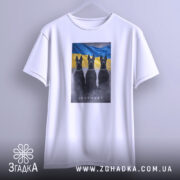 Футболка інстинкт білого кольору, підвішена на вішалці. На ній принт із трьома чорними собаками на фоні жовто-блакитного прапора. Фон світло-сірий, що створює контраст з футболкою. Принт чіткий і яскравий, з видимими деталями.