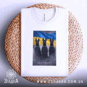 Футболка інстинкт білого кольору, складена на плетеній основі. На ній принт із трьома чорними собаками на фоні жовто-блакитного прапора. Фон натуральний, що підкреслює текстуру тканини. Принт яскравий, з чіткими деталями та написом.