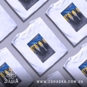 Футболка інстинкт білого кольору, зображена на моделі, яка позує з легким усмішкою. На футболці принт із трьома чорними собаками на фоні жовто-блакитного прапора. Фон з м'яким градієнтом, що підкреслює кольори. Принт детально виконаний, з видимими ланцюгами на собаках.