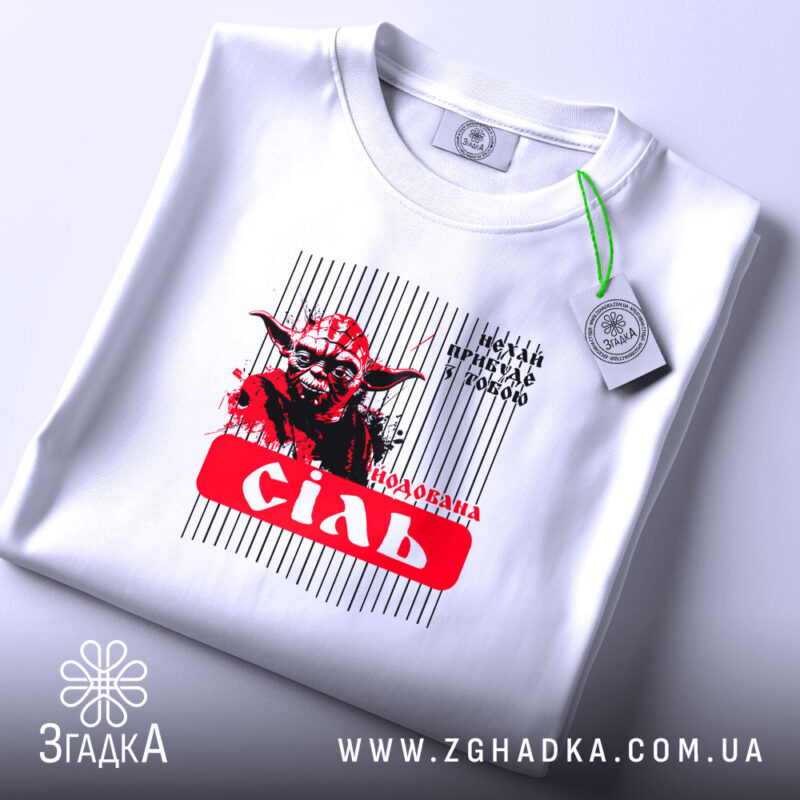 Футболка Йода Сіль, біла, з верхнього ракурсу, фон світло-сірий, принт з зображенням Йоди, текст 'подобана сіль' на червоному фоні, з етикеткою на зеленій стрічці.