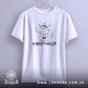 Футболка кавопивця білого кольору, підвішена на вішалці, ракурс спереду, фон світло-фіолетовий, принт з трьома чашками кави, одна з чашок з усмішкою, інша з закритими очима, текст 'КАВОПИВЕЦЬ' під принтом.