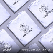 Футболка кавопивця білого кольору, зображена на молодому чоловікові, ракурс з правого боку, фон світло-фіолетовий, принт з трьома чашками кави, одна з чашок з усмішкою, інша з закритими очима, текст 'КАВОПИВЕЦЬ' під принтом.