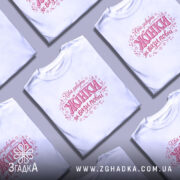 Футболка хіба ревуть жінки, біла, зображена на моделі в ракурсі спереду, фон світло-фіолетовий, принт з написом 'Хіба ревуть Жінки як вази повні' в рожевих тонах з елементами квітів.