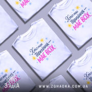 Футболка хто має терпіння, біла, зображена на моделі в ракурсі спереду, фон світло-фіолетовий, принт з текстом 'Хто має терпіння – має всіх' у кольорах синьому, рожевому та жовтому, з зірочками.