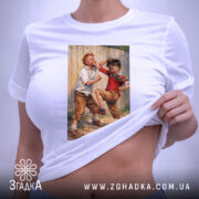 Футболка Хулігани, біла, на столі, з принтом двох хлопчиків, які граються, фон світло-сірий, деталі принта чіткі, етикетка з зеленим шнурком.