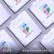 Футболка кохання це біла футболка, зображена на моделі, яка позує на нейтральному фоні. Принт на футболці містить двох анімованих персонажів: кішку і собаку, які тримаються за руки, з написом 'Кохання це...' над ними. Модель має короткі рукави і стильний крій.