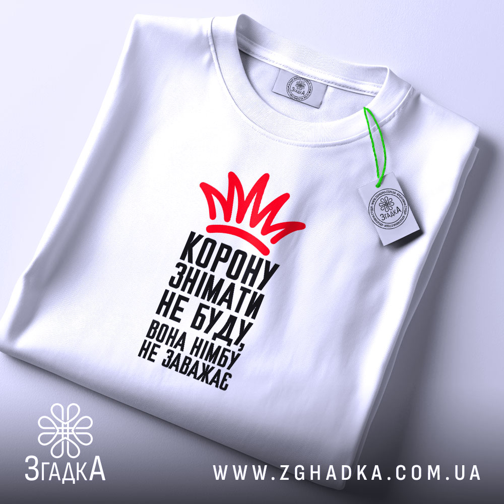 Футболка корону знімати не буду, біла футболка на плоскому фоні, зображена зверху, принт червоного кольору у вигляді корони та чорного тексту, на комірці є етикетка.
