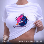 Футболка космічні пригоди Ілона, біла, на плоскій поверхні, з етикеткою, принт з космічним астронавтом, що сидить на фіолетовій планеті, з кольоровими ефектами.