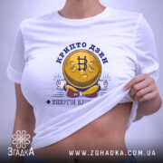 Футболка крипто дзен, біла, на плоскій поверхні, з принтом у вигляді усміхненої монети з символом біткоїна, текстом 'крипто дзен' та 'енергія блокчейну', фон світло-сірий.