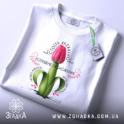 Футболка Квітка потребує зволоження. Біла футболка, розкладена на поверхні, з принтом червоного тюльпана. Фон світлий, деталі принта чітко видимі, на комірці видно етикетку.