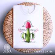 Футболка Квітка потребує зволоження. Біла футболка, складена на плетеній кошику, з принтом червоного тюльпана. Фон світлий, акцент на текстурі кошика, принт добре видно.