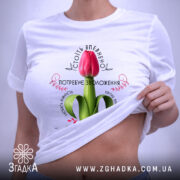 Футболка Квітка потребує зволоження. Біла футболка, розкладена на поверхні, з принтом червоного тюльпана. Фон світлий, деталі принта чітко видимі, на комірці видно етикетку.