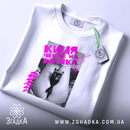 Футболка киця чекає котика. Біла футболка, зображена зверху, на фоні світло-сірого кольору. Принт з чорним котом у короні, яскравий рожевий текст, етикетка на рукаві.