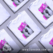 Футболка киця чекає котика. Біла футболка на молодій людині, зображена в анфас. На фоні світло-сірий колір. Принт з чорним котом у короні на фоні, з яскравим рожевим текстом.