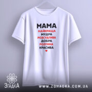 Футболка мама найкраща, біла, підвішена на вішалці, фон світло-сірий, принт чорного та червоного кольору з написом 'Мама найкраща, мудра, розсудлива, добра, розумна, красива'.