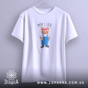 Футболка моє життя з ведмедиком, біла, на вішалці, фон світло-фіолетовий, принт ведмедика в синіх штанях і білу футболку з написом 'MY LIFE'.