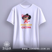 Футболка молодша сестра, біла, підвішена на вішалці, фон світло-сірий, принт з дівчинкою в червоному вбранні з чорними кучерями, тримає тризубець, текст 'молодша сестра' жовтого кольору.