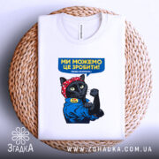 Футболка ми можемо це зробити, біла, на плетеній основі, фон світло-сірий, принт з чорним котом у червоній бандані, що піднімає кулак, текст на футболці синій з жовтим.