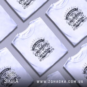 Футболка наче мольфара послала, біла, зображена з близького ракурсу на моделі, фон світло-фіолетовий, принт чорного кольору з текстом та декоративними елементами.