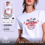 Футболка найкраща дружина. Біла футболка з коротким рукавом, зображена в ракурсі спереду, на фоні світло-сірого кольору. Принт червоного кольору з чорними елементами, напис "Найкраща дружина у світі" оточений декоративними сердечками та візерунками.