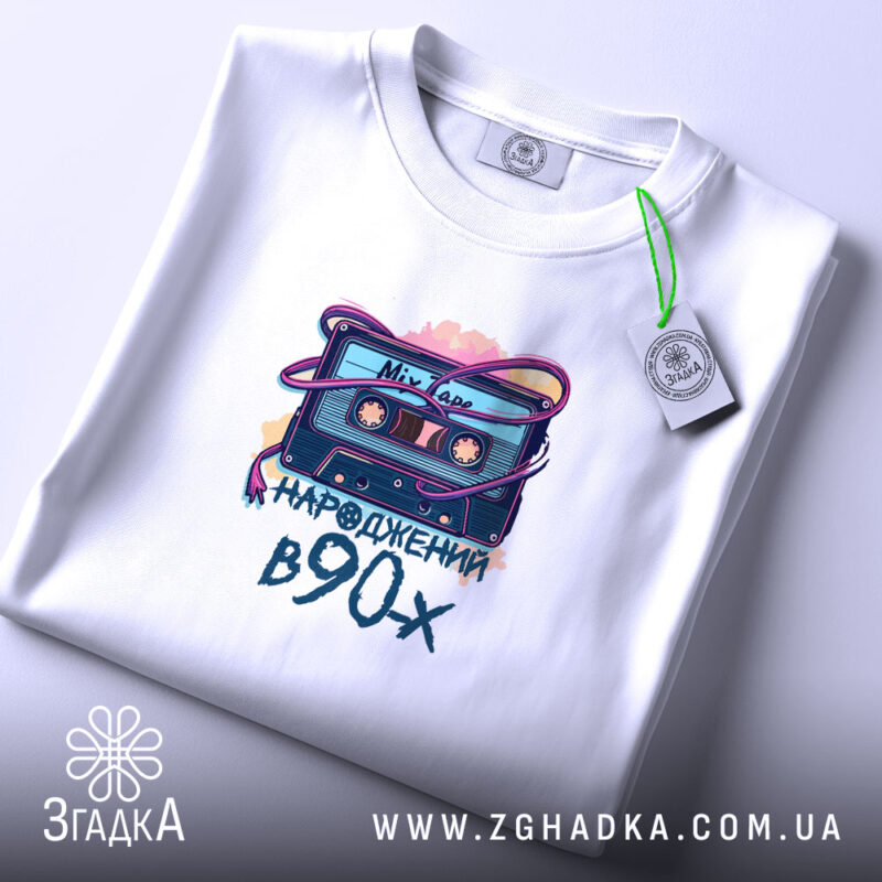 Футболка народжений у 90-х стиль, біла, на столі, з етикеткою, принт з касетою та написом 'народжений в 90-х' на передній частині, фон світлий.