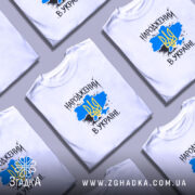 Футболка народжений в Україні, біла, на моделі, з фоном у світло-фіолетових тонах, принт з жовто-блакитним тризубом на синьому фоні, текст "НАРОДЖЕНИЙ В УКРАЇНІ" виконаний у чорному кольорі.