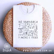 Футболка не хвилюйся у мене є план. Біла футболка, складена на плетеній основі, з видимим принтом. На фоні світло-сірий колір. Принт чорного кольору з математичними формулами та написом 'НЕ ХВИЛЮЙСЯ У МЕНЕ Є ПЛАН'.