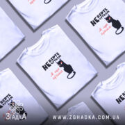 Футболка не вірте чуткам, біла, зображена на моделі, фон світло-фіолетовий, принт з чорним котом та текстом у чорному і червоному кольорах.