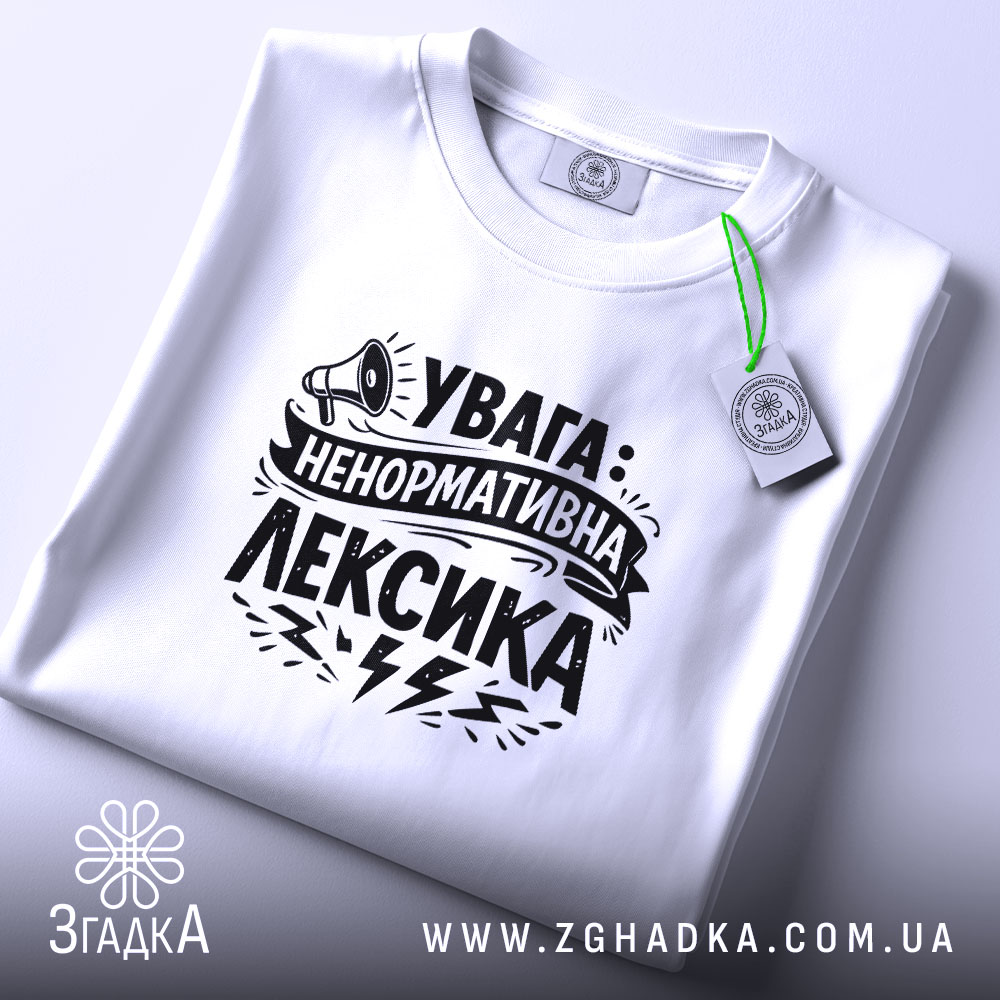 Футболка ненормативна лексика, біла, на столі, фон світло-сірий, принт чорний з написом 'УВАГА: НЕНОРМАТИВНА ЛЕКСИКА' та малюнком гучномовця, з етикеткою.