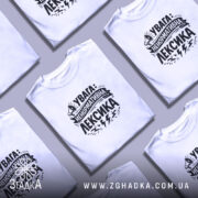 Футболка ненормативна лексика, біла, на моделі, фон світло-сірий, принт чорний з написом 'УВАГА: НЕНОРМАТИВНА ЛЕКСИКА' та малюнком гучномовця.