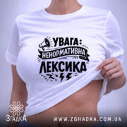 Футболка ненормативна лексика, біла, на столі, фон світло-сірий, принт чорний з написом 'УВАГА: НЕНОРМАТИВНА ЛЕКСИКА' та малюнком гучномовця, з етикеткою.