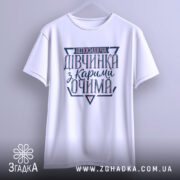 Футболка непосидюча дівчинка, білого кольору, зображена з фронтального ракурсу на світло-сірому фоні, принт на футболці містить текст "непосидюча дівчинка з карими очима" в темно-синіх та рожевих відтінках.