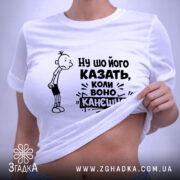 Футболка ну шо його казать, біла футболка, складена на поверхні, з принтом, що містить персонажа з сумним виразом обличчя та текстом "Ну шо його казать, коли воно канешно". На футболці є етикетка з зеленим шнурком. Фон світло-сірий.