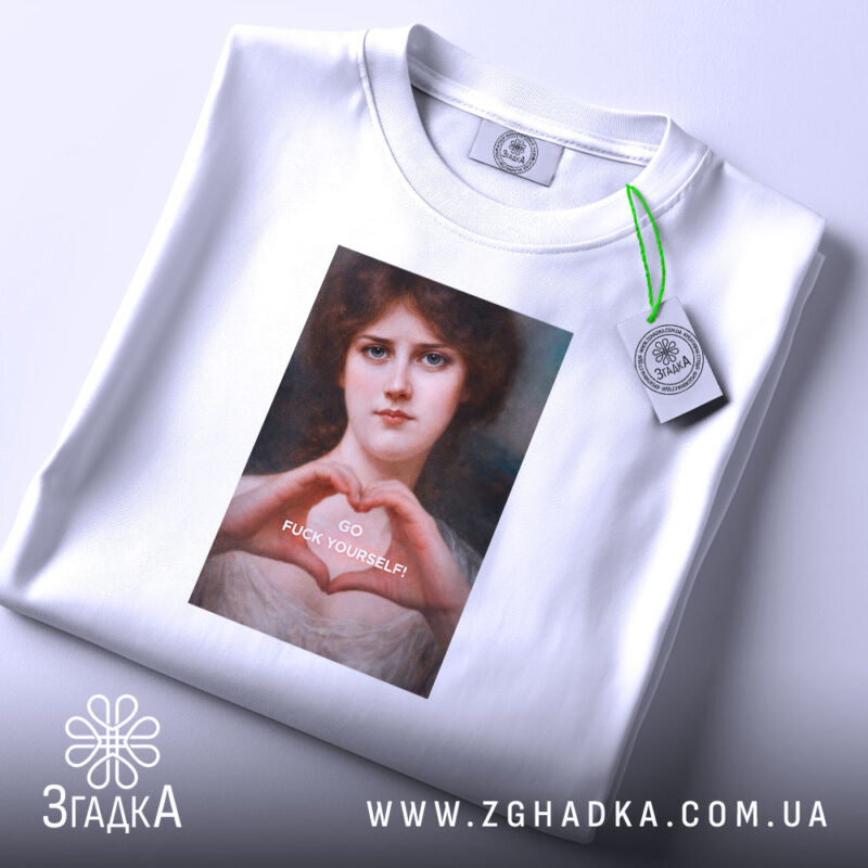 Футболка-оберіг від ідіотів, біла футболка, розкладена на поверхні, з принтом жінки, що формує серце руками, на фоні світлого кольору, з етикеткою, що звисає з коміра.