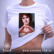Футболка-оберіг від ідіотів, біла футболка, розкладена на поверхні, з принтом жінки, що формує серце руками, на фоні світлого кольору, з етикеткою, що звисає з коміра.
