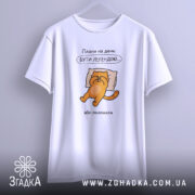 Футболка плани на день: біла футболка з коротким рукавом, зображення оранжевого кота на подушці, текст "Плани на день: БУТИ ЛЕГЕНДОЮ...". Футболка підвішена на світлому фоні, акцент на принті.