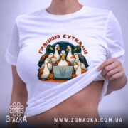 Футболка працюю сутками, біла, зображена на столі, ракурс зверху, фон світло-фіолетовий, принт з птахами навколо ноутбука, з написом 'ПРАЦЮЮ СУТКАМИ', на етикетці зелена стрічка.