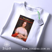 Футболка проти непроханих порад. Біла футболка на столі, знята зверху, фон світлий. Принт з портретом жінки в червоній сукні, текст на принті чорний з червоним, запитує: 'Чи я вбиса запитувала вашу думку?'.