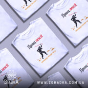 Футболка принц пенсії, біла, зображена на чоловікові, який позує на світлому фоні, принт з чорним силуетом персонажа з червоною палицею та текстом 'Принц пенсії' у верхній частині.