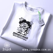 Футболка принцеса пенсії, біла, на столі, з верхнього ракурсу, фон світло-сірий, принт з карикатурою жінки з котами, текст під принтом: 'Котів забагато не буває.'