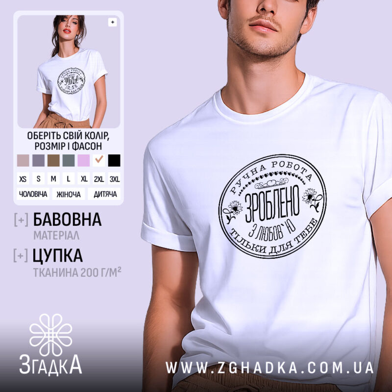 Футболка ручна робота з любов’ю, біла, на моделі з легким усмішкою, фон світло-фіолетовий, принт чорного кольору з текстом та квітковими елементами.