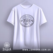 Футболка ручна робота з любов’ю, біла, підвішена на вішалці, фон світло-сірий, принт чорного кольору з текстом та квітковими елементами, видно округлі рукави.