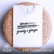 Футболка шукаю парубка, біла, складена на плоскій поверхні, оточена плетеним кошиком, принт чорного кольору з текстом, що говорить про пошук хорошого парубка.