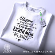Футболка шукаю того самого, біла, складена на поверхні, фон світло-сірий, принт чорний з текстом, на комірці є етикетка.