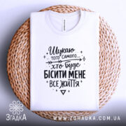 Футболка шукаю того самого, біла, складена на плетеній основі, фон світло-сірий, принт чорний з текстом, видно комірець.