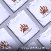 Футболка слід сили природи, біла, на моделі, з легким макіяжем, фон світло-фіолетовий, принт коричневого кольору з ведмедем та деревами.