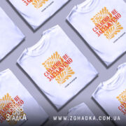 Футболка слухаємо і не засуджуємо, біла, зображена на моделі, фон світло-фіолетовий, принт жовтий з рослинним орнаментом та червоним текстом.