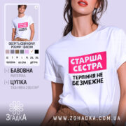 Футболка старша сестра, біла, на моделі, з фоном у світло-фіолетових тонах, принт з написом 'Старша сестра' у рожевому прямокутнику та 'Терпіння не безмежне' чорним шрифтом.